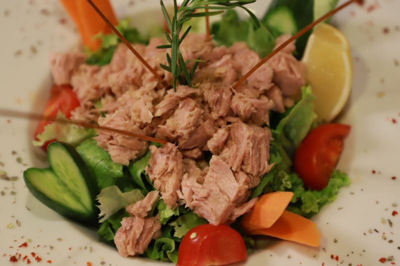 Illustrative tuna salad over lettuce and tomatoes with a lemon wedge.