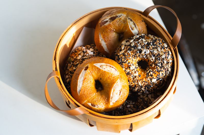 Illustrative plain and seeded bakery bagels in a wooden basket.