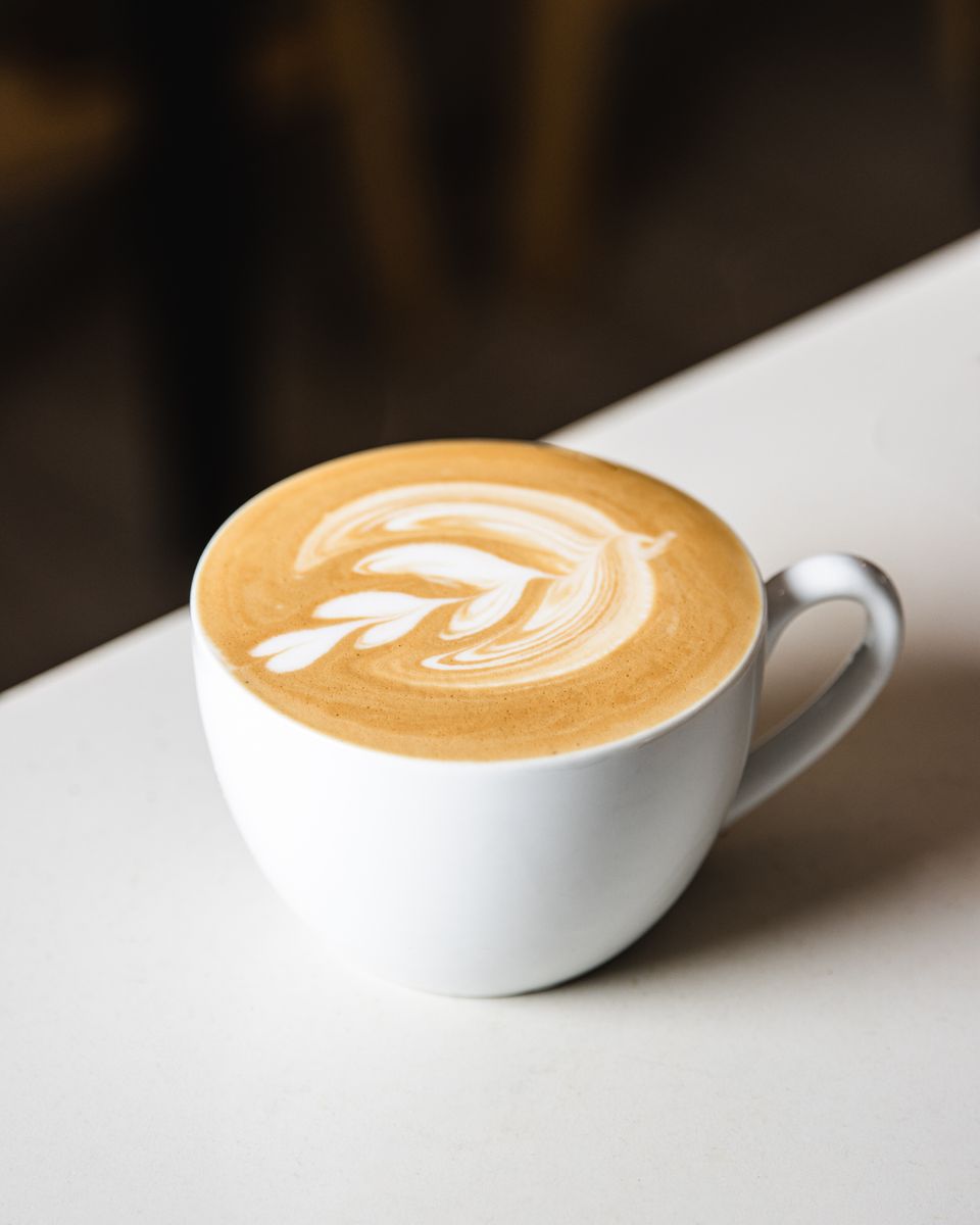 Illustrative photo of a cafe latte with leaf-shaped milk art in a white ceramic cup.