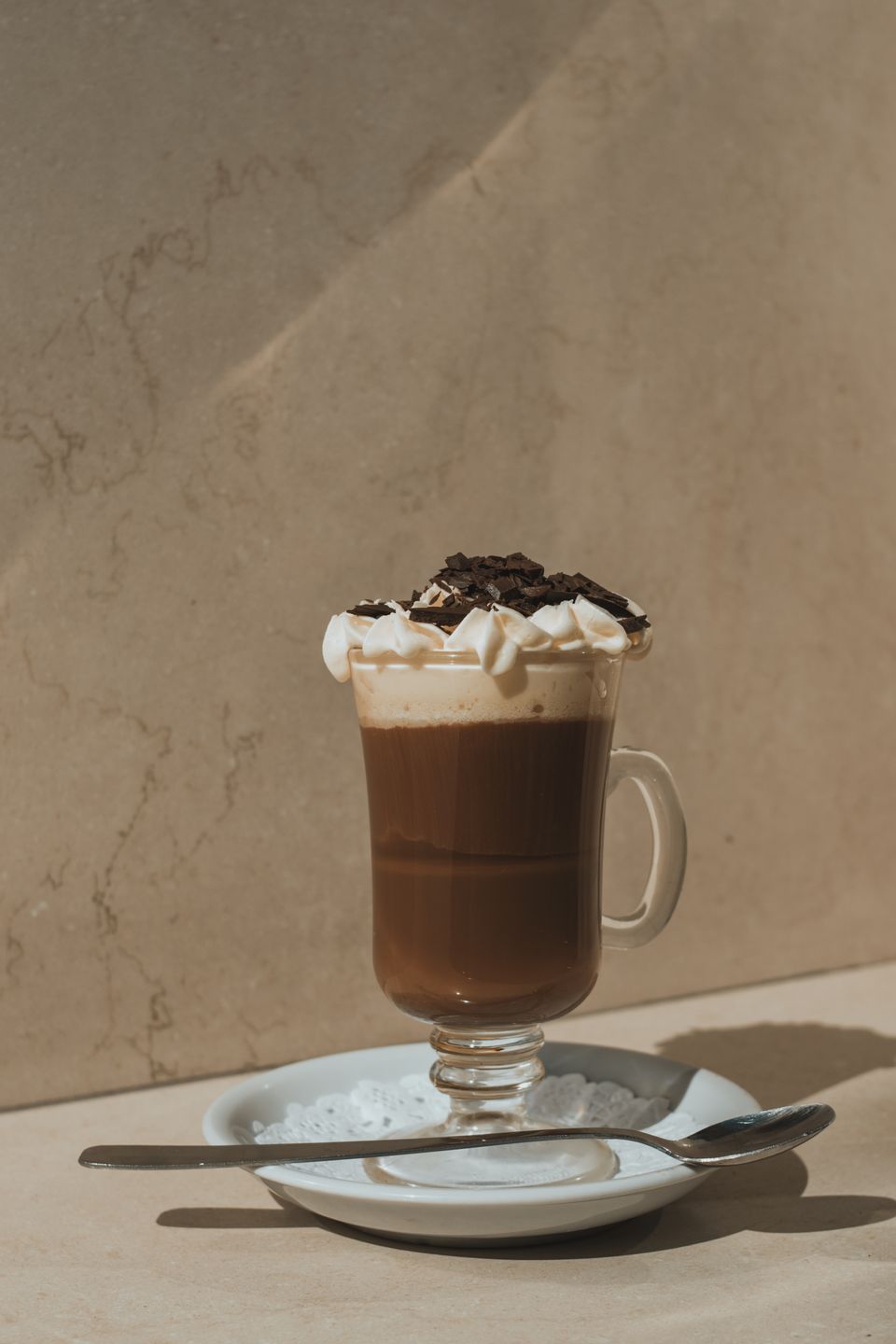 Illustrative photo of a mocha in a glass mug with cream and chocolate shavings.