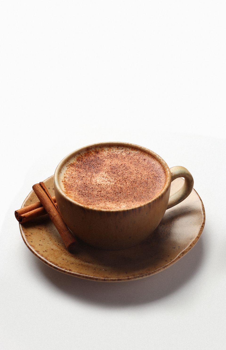 Illustrative photo of a warm spiced chai latte in a ceramic cup beside cinnamon sticks.