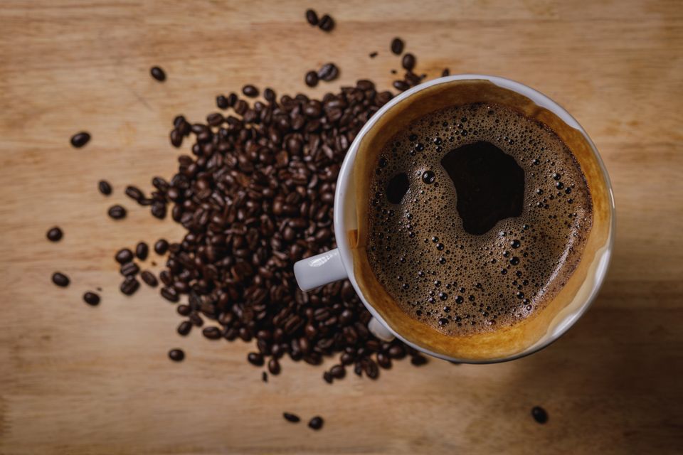 Illustrative photo of black coffee in a white cup beside roasted coffee beans.