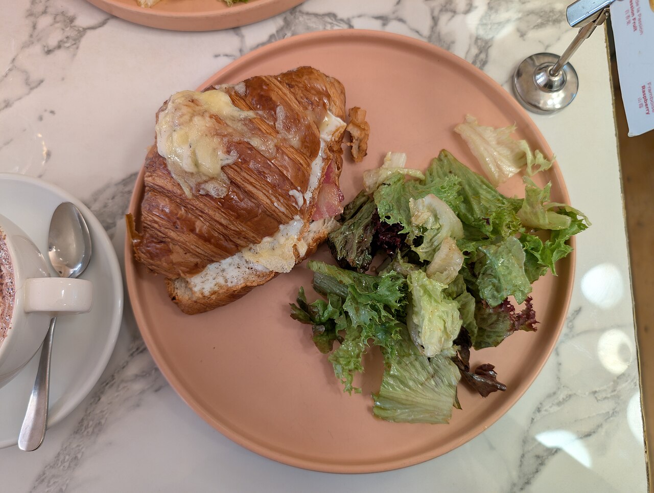 Illustrative photo of a bacon and egg croissant sandwich with a side salad.