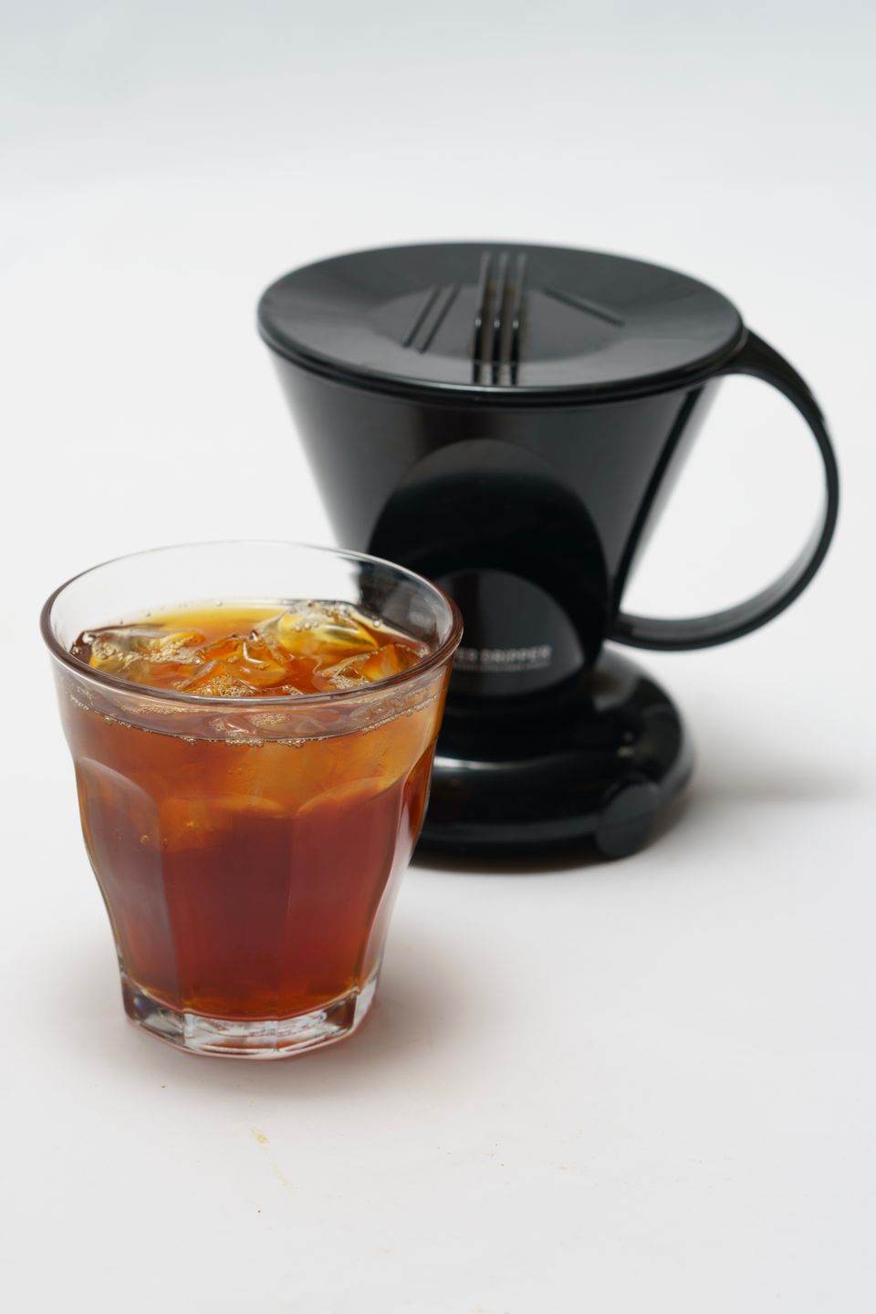 Illustrative photo of black coffee over ice in a clear glass beside a coffee dripper.