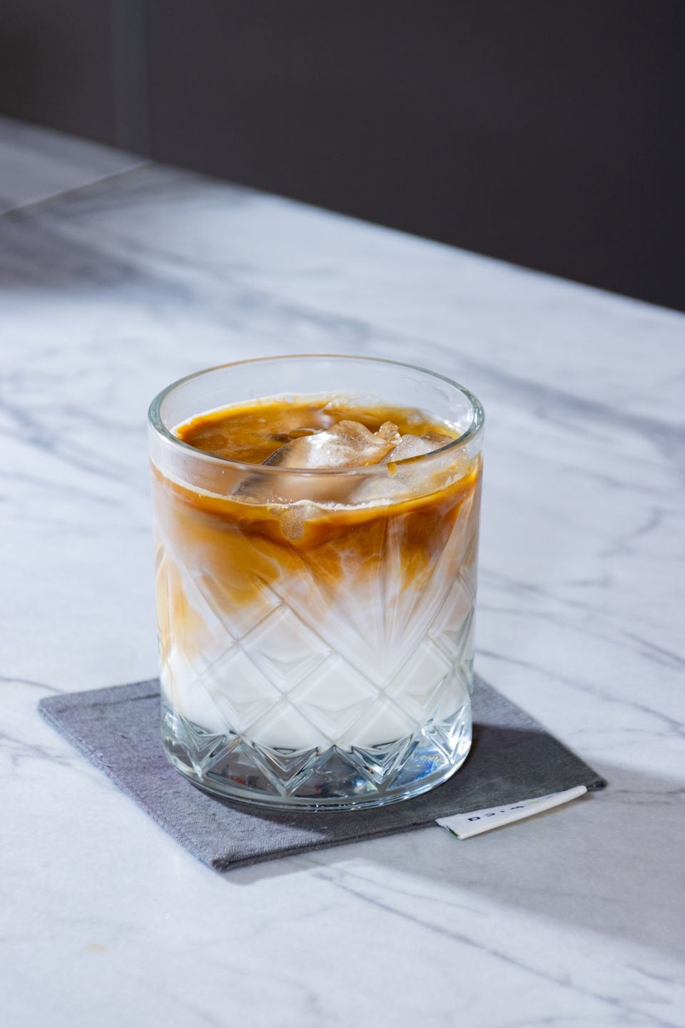 Illustrative photo of an iced latte with coffee, milk and large ice cubes in a patterned glass.