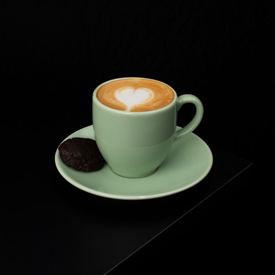 Illustrative photo of an espresso macchiato with a small white milk heart in a pale green cup.