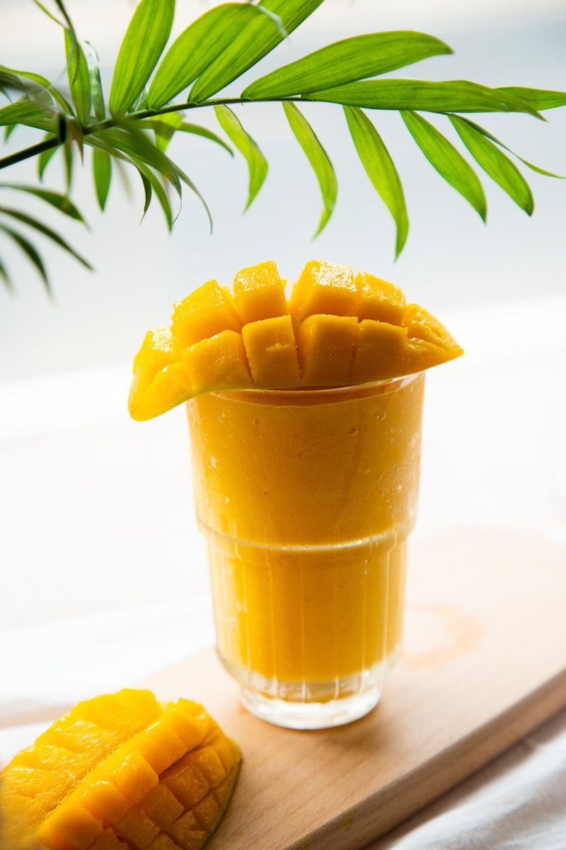 Illustrative golden mango smoothie in a glass with fresh mango garnish.