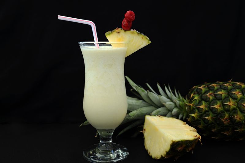Illustrative creamy piña colada style drink with a pineapple wedge and straw.