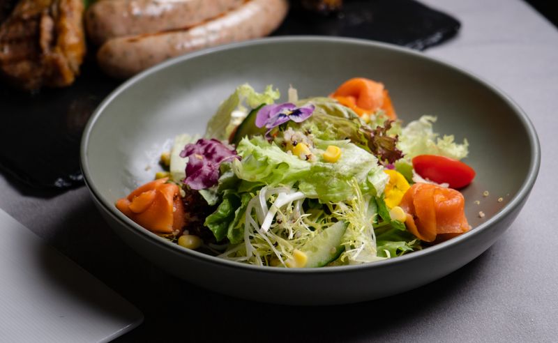Illustrative smoked salmon salad with mixed leaves and tomatoes in a gray bowl.