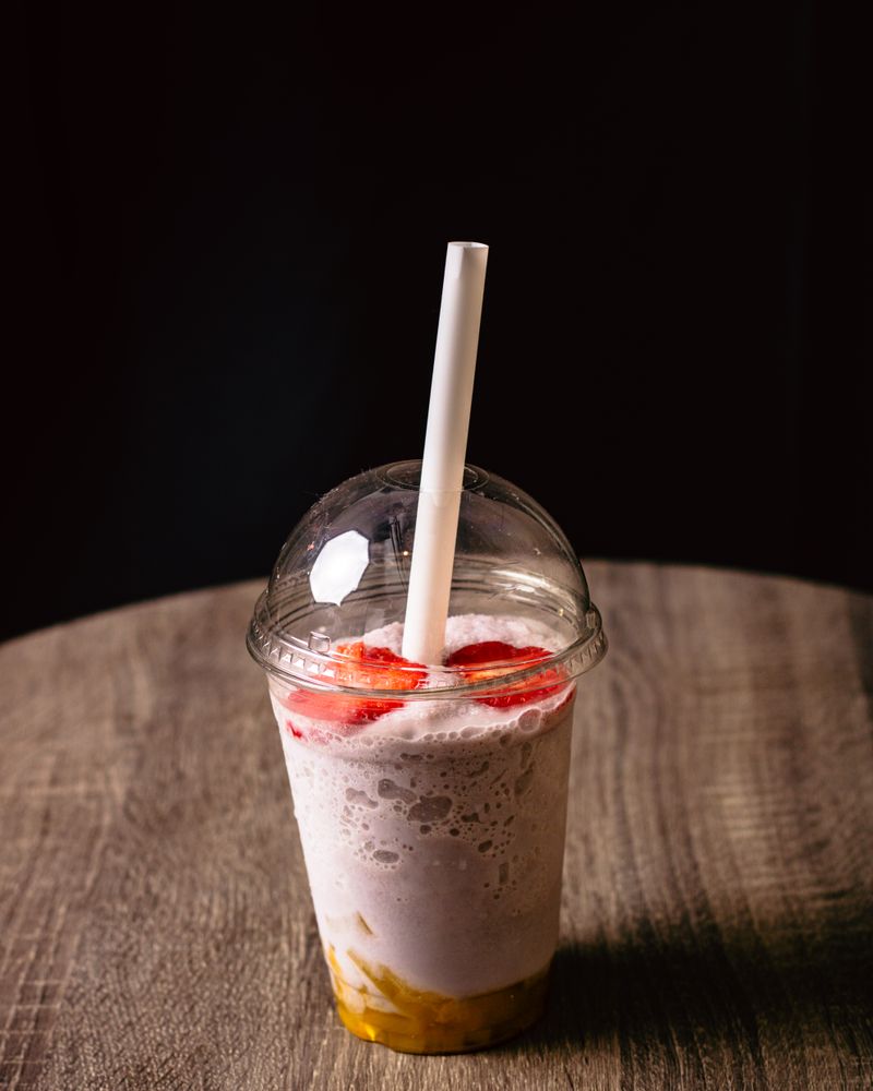 Illustrative strawberry banana smoothie in a clear takeaway cup with a straw.