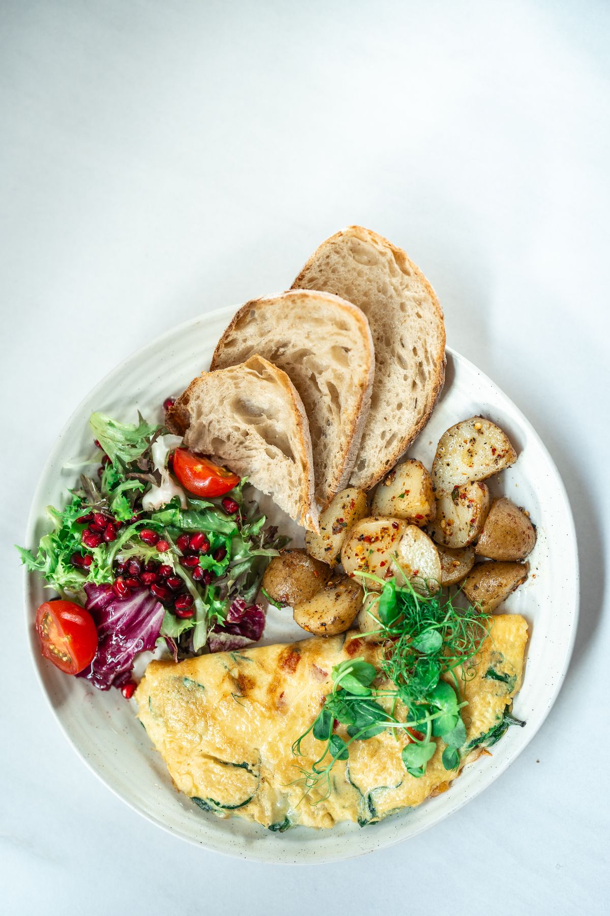 Illustrative photo of a folded omelette with greens, accompanied by salad, bread and potatoes.