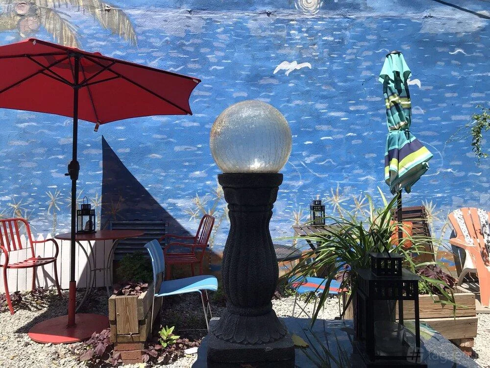 Patio tables, umbrellas, plants and a garden light in front of the blue mural.