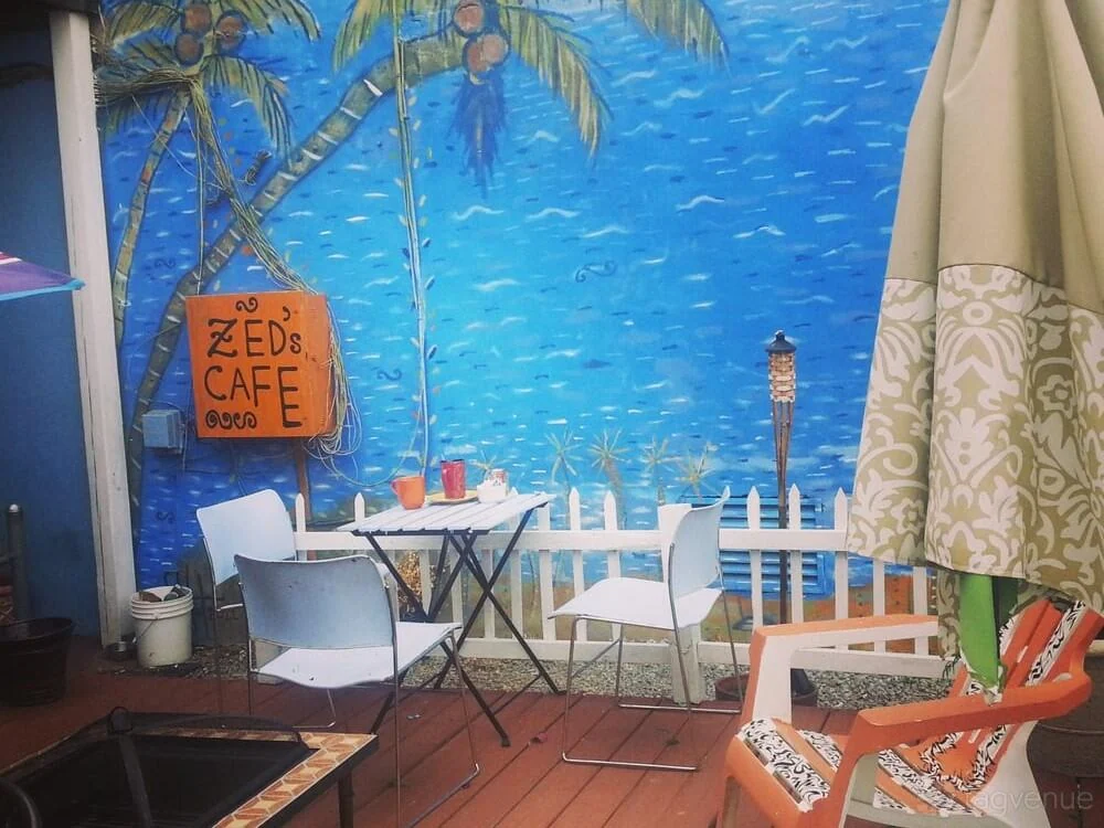 Zed’s Cafe sign, tables and chairs beside the blue patio mural.
